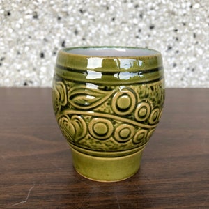 Puede incluir: Una taza de cerámica verde con un diseño en relieve de círculos y espirales.