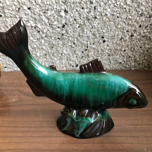 May include: A green and brown glazed ceramic fish figurine. The fish is in a leaping pose with its tail raised. The base of the figurine is shaped like a wave.