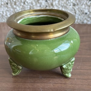 May include: A green ceramic incense burner with a brass rim and three decorative feet.
