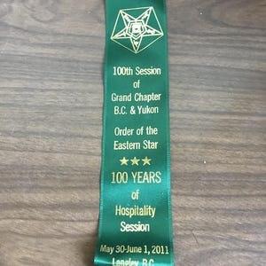 May include: Green ribbon with gold lettering announcing the 100th Session of the Grand Chapter B.C. & Yukon Order of the Eastern Star. The ribbon also states "100 YEARS of Hospitality Session" and "May 30-June 1, 2011 Langley, B.C."