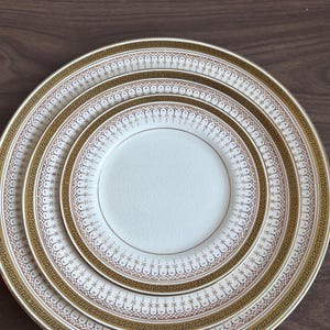 Könnte beinhalten: Ein Stapel feiner Porzellanteller mit cremefarbenem Mittelteil und einem gold-braunen Zierrand. Die Teller sind in absteigender Reihenfolge angeordnet und zeigen ein klassisches und elegantes Design.