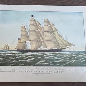 Peut inclure: Une estampe vintage du Clipper Ship "Flying Cloud" naviguant sur l'océan. Le navire a plusieurs voiles et un drapeau américain. Du texte est présent en bas, et un autre navire est visible au loin.