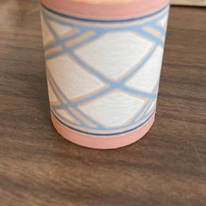 May include: A roll of pink and blue patterned wallpaper trim. The trim features a geometric design with white squares and blue lines. The roll is labeled "20¢ TRIM 15¢".