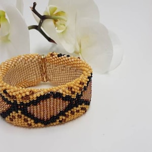 Könnte beinhalten: Ein Armband aus Perlen mit einem Schlangenhautmuster in Braun-, Schwarz- und Goldtönen.