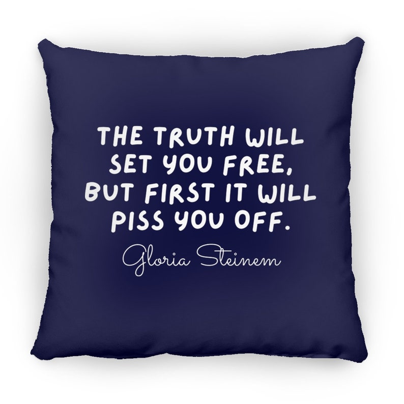 May include: A navy blue throw pillow with white text that reads "THE TRUTH WILL SET YOU FREE, BUT FIRST IT WILL PISS YOU OFF."  The text is in a handwritten font.  The author's name, "Gloria Steinem", is written in cursive below the quote.