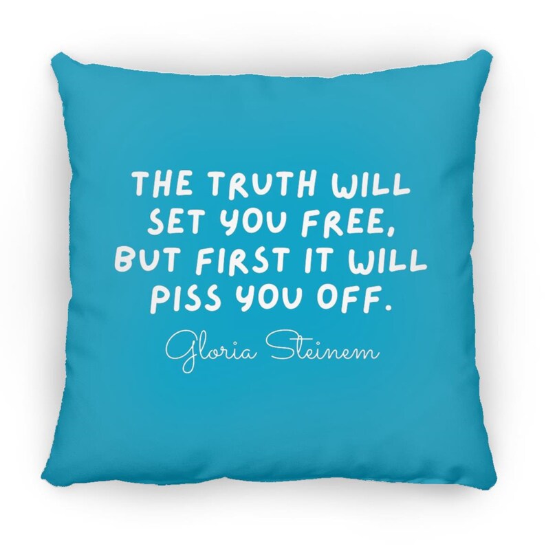 May include: A turquoise blue throw pillow with white text that reads "THE TRUTH WILL SET YOU FREE, BUT FIRST IT WILL PISS YOU OFF." The text is in a handwritten font. The author's name, "Gloria Steinem", is written in cursive below the text.