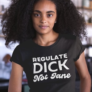 May include: A black t-shirt with white text that reads "Regulate Dick Not Jane".