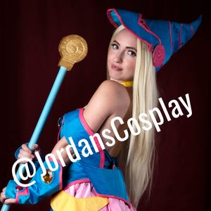 Può includere: Un costume cosplay blu e rosa, che include un vestito e un cappello. Il costume presenta un bastone con un'orbita dorata. Il testo "@jordansCosplay" è sovrapposto all'immagine.