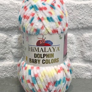 May include: A ball of Himalaya Dolphin Baby Colors yarn. The yarn is white with flecks of red, blue, and yellow. The label reads "Himalaya Dolphin Baby Colors". The yarn is soft and plush, suitable for baby projects.