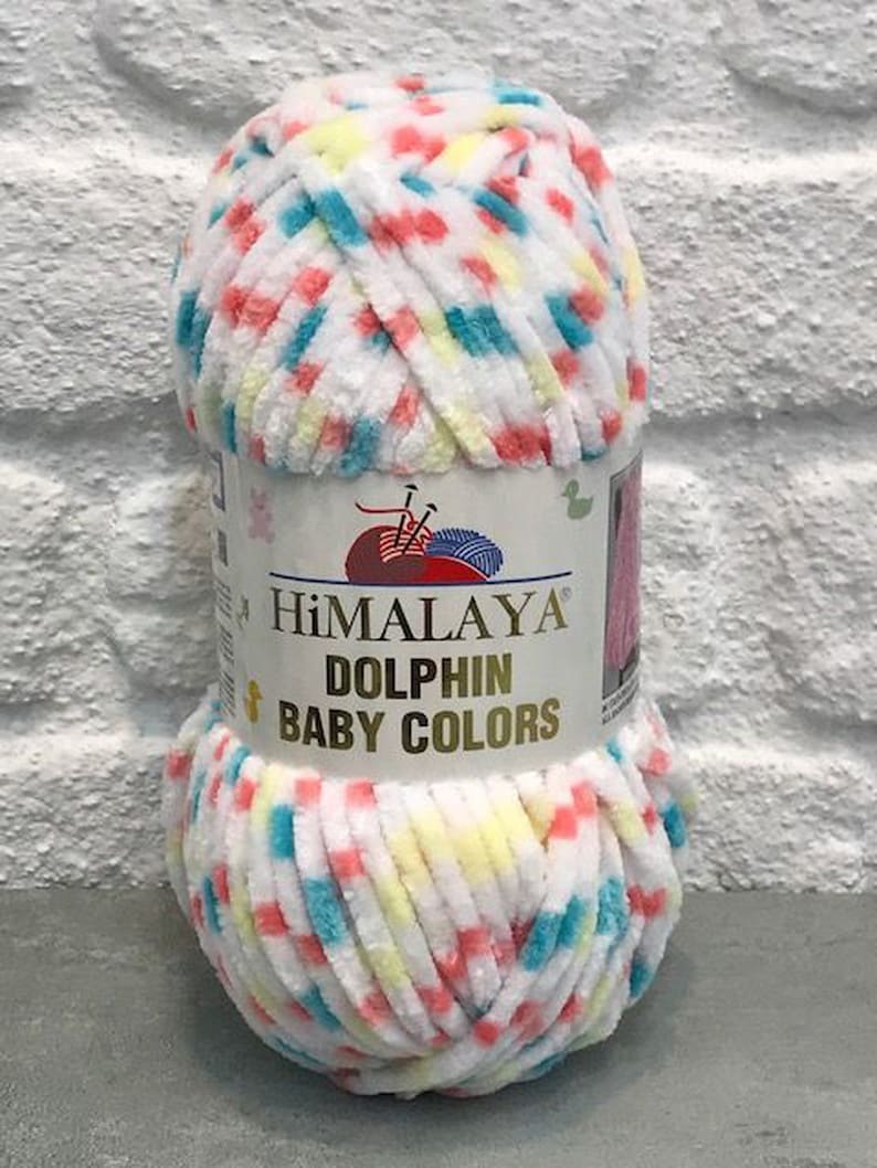 May include: A ball of Himalaya Dolphin Baby Colors yarn. The yarn is white with flecks of red, blue, and yellow. The label reads "Himalaya Dolphin Baby Colors". The yarn is soft and plush, suitable for baby projects.