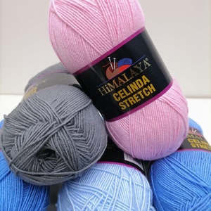 Może przedstawiać: Kolekcja kolorowych motków przędzy, w tym różowy, szary, jasnoniebieski i niebieski. Różowy motek jest w centrum, z etykietą "Himalaya Celinda Stretch". Przędza jest ułożona w stos, sugerując projekt rzemieślniczy lub dziewiarski.