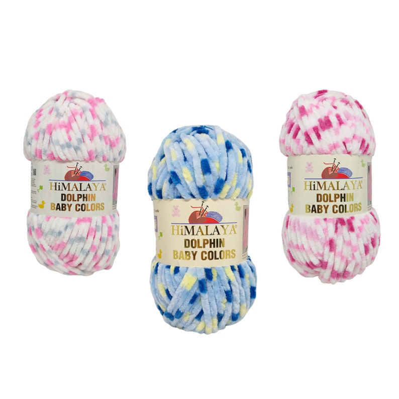 May include: Three balls of Himalaya Dolphin Baby Colors yarn in pink, blue, and white. Each ball has a label with the brand name and product details. The yarn appears soft and plush, suitable for baby projects.