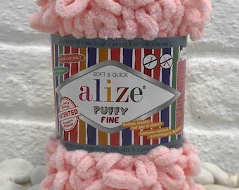 May include: A skein of light pink Alize Puffy Fine yarn with a looped texture. The central paper label features the text Alize Puffy Fine, Soft & Quick, and Patented, set against a background of vertical multicolored stripes.