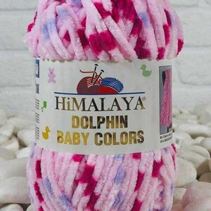 May include: A ball of Himalaya Dolphin Baby Colors yarn in pink, fuchsia, and light blue. The label displays the brand name and product details. The yarn is fluffy and soft, suitable for baby projects.