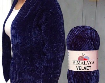 May include: A navy blue velvet cardigan with a cable knit design is displayed next to a ball of matching yarn. The yarn label reads "Himalaya Velvet". The cardigan is open-fronted and has a soft, plush texture.