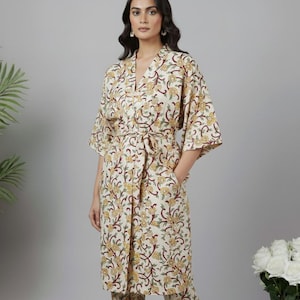 Pode incluir: Conjunto de roupão e calças a condizer com estampado floral creme. O roupão tem decote em V, cinto na cintura e bolsos, e calças de perna reta. O padrão floral inclui detalhes em amarelo e bordô. O conjunto é adequado para relaxar ou dormir.