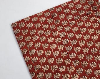 May include: Red fabric with a white floral pattern. The fabric has a small-scale, repeating pattern of white flowers and leaves on a red background.