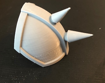 Op de afbeelding: Een grijs 3D-geprint helm met twee puntige spikes aan de bovenkant.