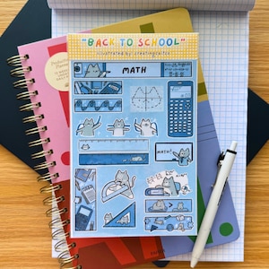 Könnte beinhalten: Eine Sammlung von Schulmaterialien, darunter Notizbücher, ein Stift und ein Stickerbogen. Der Stickerbogen zeigt Mathe-Illustrationen mit Katzen und den Text "BACK TO SCHOOL" und "MATH". Die Notizbücher sind in verschiedenen Farben, darunter Rosa, Blau und Schwarz.