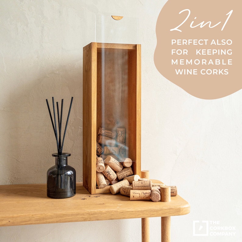 May include: A wooden wine cork holder with a clear acrylic top. The holder is filled with wine corks and is sitting on a wooden table. The text "2 in 1 PERFECT ALSO FOR KEEPING MEMORABLE WINE CORKS" is visible in the image.