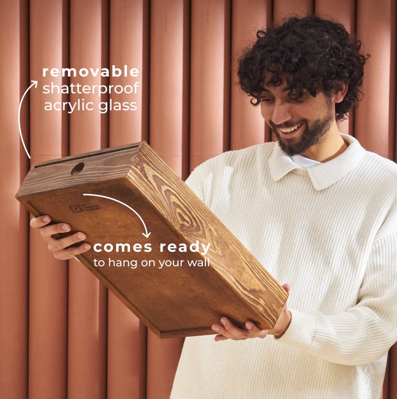 May include: A person holds a wooden frame with a removable shatterproof acrylic glass panel. The frame is ready to hang on a wall.