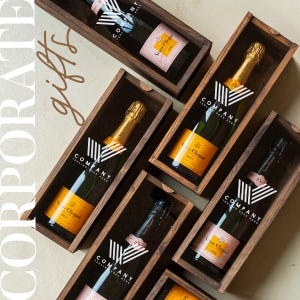 May include: A collection of wooden gift boxes with clear lids, each containing a bottle of champagne. The boxes are decorated with a white and black striped design and the text "COMPANY TAGLINE GOES HERE".