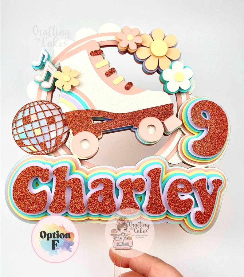 May include: A colorful cake topper featuring a roller skate, disco ball, flowers, and the name "Charley" in glittery letters. The number "9" is also included. The topper has a rainbow theme and is designed for a birthday celebration.