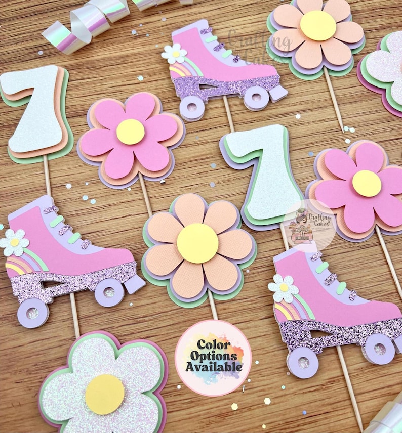 May include: A collection of colorful paper cutouts, including roller skates, flowers, and the number seven. The roller skates are pink with glitter accents and rainbow details. The flowers have layered petals in shades of pink, peach, and green.