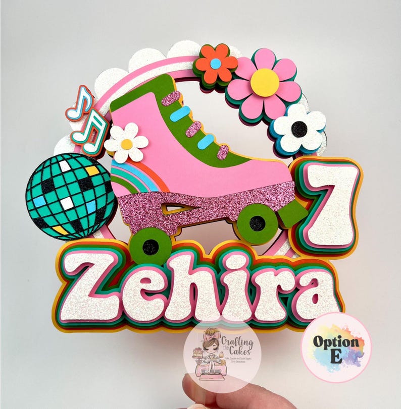 May include: A colorful cake topper featuring a pink roller skate with glitter accents, flowers, and a disco ball. The name "Zehira" and the number "7" are prominently displayed. The design has a retro theme.