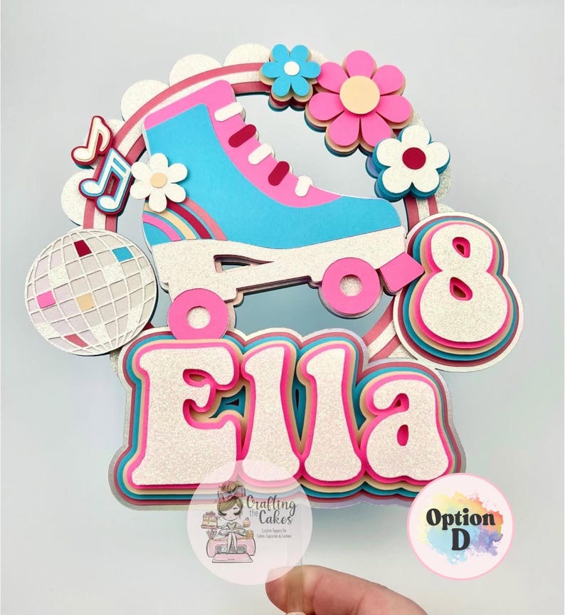 May include: A layered cake topper featuring a pink and blue roller skate, flowers, a disco ball, and the name "Ella" in a retro font. The number "8" is also included. The design is accented with glitter and rainbow details.