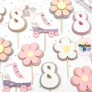 May include: A collection of pastel-colored cake toppers, including flowers, the number 8, and roller skates. The toppers are made of layered paper and glitter, with wooden sticks for insertion into cakes. The color palette includes pink, yellow, and white.
