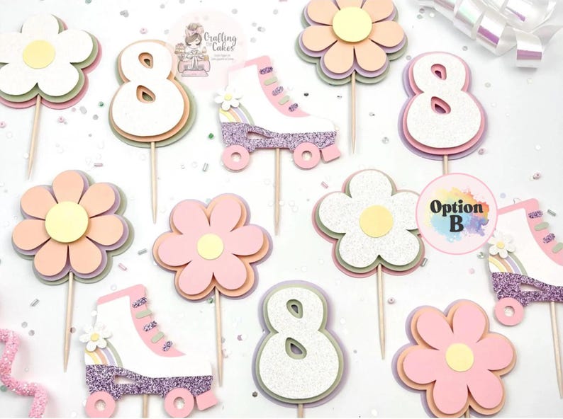 May include: A collection of pastel-colored cake toppers, including flowers, the number 8, and roller skates. The toppers are made of layered paper and glitter, with wooden sticks for insertion into cakes. The color palette includes pink, yellow, and white.