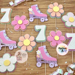 May include: A collection of decorative cupcake toppers featuring pink roller skates, flowers, and the number 7. The roller skates have glitter accents and small rainbows. The flowers are layered with pastel colors. The toppers are on wooden sticks.