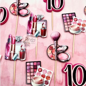 May include: Pink and black makeup-themed cake toppers. The toppers include lipstick, perfume, eyeshadow palettes, blush, makeup brushes, and the number 10. The background is a watercolor wash of pink.
