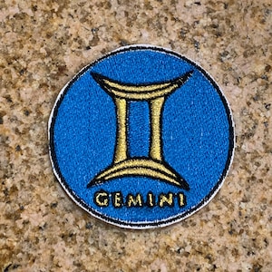 Puede incluir: Un parche de hierro bordado en azul y dorado con el símbolo del zodíaco Géminis y la palabra "GEMINI" en letras doradas.