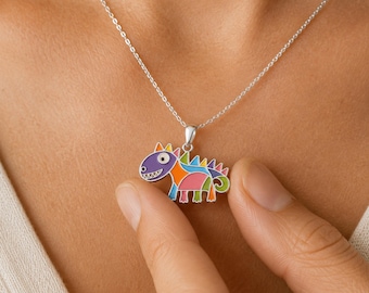 Könnte beinhalten: Eine silberfarbene Halskette mit einem Anhänger in Form eines stilisierten Dinosauriers. Der Dinosaurier-Anhänger ist mit leuchtenden Emaille-Abschnitten in Lila, Blau, Pink, Orange und Grün verziert und hat weiße Details an Auge und Zähnen.