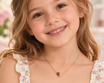 Könnte beinhalten: Eine goldene Halskette mit einem kleinen herzförmigen Anhänger, der auf einer Seite einen roten Edelstein und auf der anderen einen klaren weißen Edelstein aufweist. Die Kette wird um den Hals getragen. Der Text Paws & Knight ist unten rechts sichtbar.
