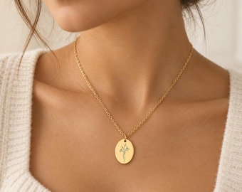 Könnte beinhalten: Eine goldfarbene Halskette mit einem zierlichen ovalen Anhänger. Der Anhänger ist mit einer feinen Linienzeichnung einer Schneeglöckchenblume graviert. Die Kette besteht aus einer dünnen, passenden goldfarbenen Gliederkette mit runden Gliedern.