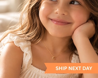 Puede incluir: Un collar de tono dorado con un pequeño colgante de letra C en una cadena delicada. La pieza se lleva alrededor del cuello, mostrando un diseño minimalista con un acabado pulido. El texto SHIP NEXT DAY y PAWS & KNIGHT son visibles.