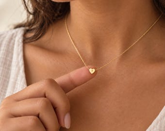 Könnte beinhalten: Eine goldfarbene Halskette mit einer zarten Kette und einem kleinen herzförmigen Anhänger. In die Mitte des Herzens ist die Zahl 7 eingraviert. Die Kette wird um den Hals getragen und der Anhänger liegt auf der Haut auf.