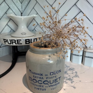 Puede incluir: Un tarro de cerámica gris con letras azules que dicen "MOUTARIDE DE DIJON EXTRA FORTE BOCQUET PREPAREE AU VINAIGRE YVETOT (S.I)". El tarro está lleno de flores secas.