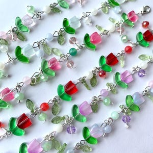 May include: A set of six delicate bracelets featuring a floral design with green leaves and colorful glass tulips. The bracelets are made with silver chain and various colored beads.