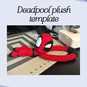 May include: A red Deadpool plush toy with black accents, lying on a cutting mat. The plush has a white-eyed mask and is in a relaxed pose. Text on the image reads "Deadpool plush template".
