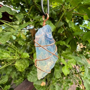 May include: A clear, iridescent crystal pendant wrapped in copper wire, hanging from a black cord. The pendant is a unique and eye-catching piece of jewelry.