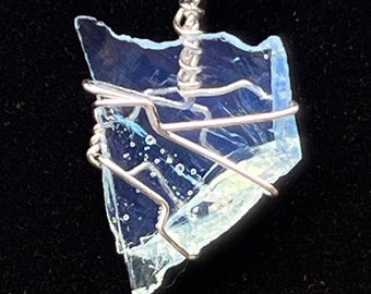 May include: A silver wire wrapped pendant featuring a blue and clear iridescent glass shard. The pendant is hanging from a black cord.