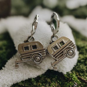 Puede incluir: Un par de pendientes de plata con un dije de caravana. Los pendientes son de aro con acabado plateado.