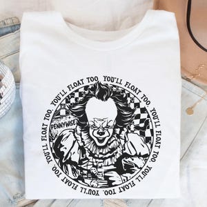 May include: White t-shirt with a black and white graphic of Pennywise the clown from the movie "IT". The graphic features the text "You'll float too" repeated around the edge of the circle.
