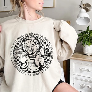 May include: A cream-colored sweatshirt with a black and white graphic of a character from the movie Child's Play. The graphic includes the text "I'm your friend til the end. I'm your friend til the end." and "Chucky".