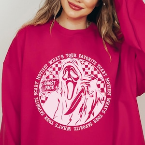 May include: Pink sweatshirt with a white circle graphic featuring a ghost face with a knife and the text "WHAT'S YOUR FAVORITE SCARY MOVIES? WHAT'S YOUR FAVORITE SCARY MOVIES?" and "GHOST FACE".