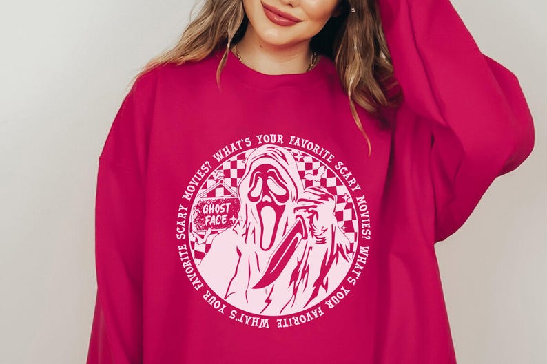 May include: Pink sweatshirt with a white circle graphic featuring a ghost face with a knife and the text "WHAT'S YOUR FAVORITE SCARY MOVIES? WHAT'S YOUR FAVORITE SCARY MOVIES?" and "GHOST FACE".